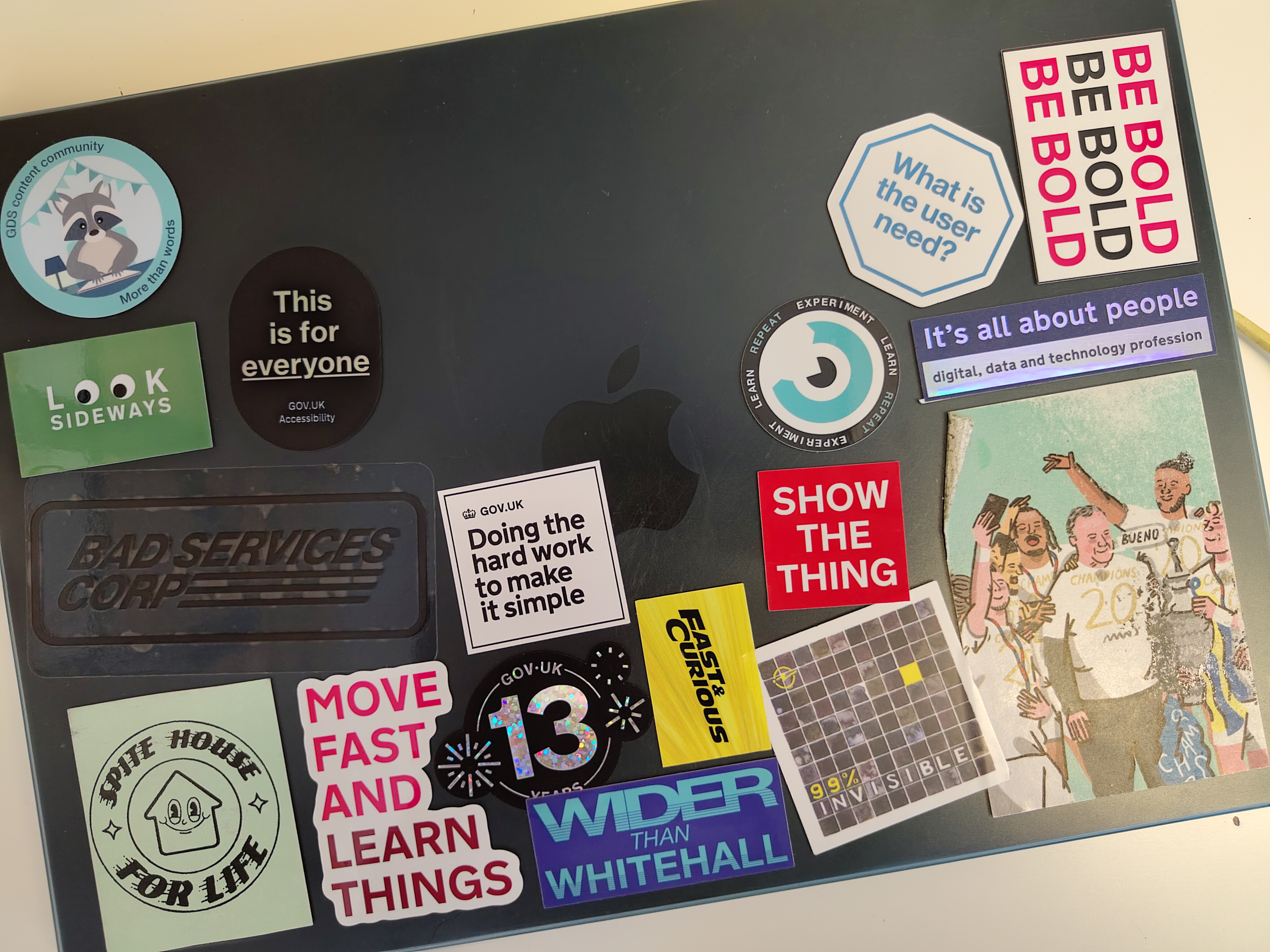  The top of a MacBook Air laptop, covered in stickers related to the Government Digital Service. These include some reading: 'GDS Content Community: More than words', 'Look sideways', 'This is for everyone', 'Be bold, be bold, be bold', 'Doing the hard work to make it simple', 'Move fast and learn things', 'Fast and curious', 'Show the thing', 'What is the user need?', 'It's all about people'.